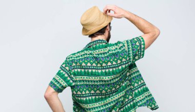 Genç turist düşünüyor ya da şüphe ediyor, kafasını kaşıyor, kafası karışık ve kafası karışık hissediyor, beyaz duvarın arkasında ya da arkasında.