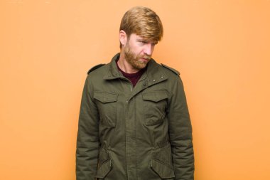 Genç sarışın adam üzgün, üzgün ya da kızgın ve olumsuz bir tavır takınıyor düz duvara karşı anlaşmazlık içinde.