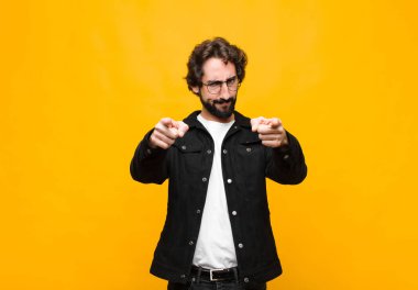 Genç, deli, yakışıklı bir adam kameraya hem parmaklarını hem de suratını doğrultup turuncu duvara karşı görevini yapmanı söylüyor.