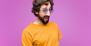 Genç, çılgın, havalı bir adam, büyük, dost canlısı, kaygısız bir gülümsemesi var, pozitif görünüyor, rahat ve mutlu, düz duvara karşı takılıyor.