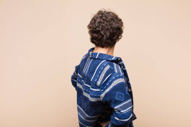 Genç, çılgın, havalı bir adam kafası karışık ya da şüpheci ve soru dolu, merak ediyor, elleri kalçasında, düz duvara karşı dikiz manzaralı