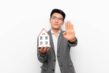 Genç Japon bir adam ciddi, sert, hoşnutsuz ve kızgın görünüyor. Bir ev mankeniyle el hareketini durduruyor.