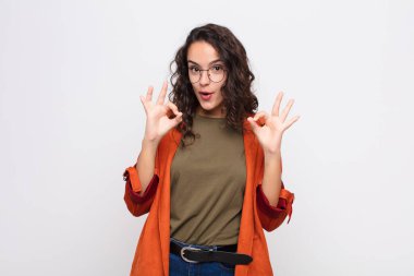 Genç, güzel bir kadın şok olmuş, şaşırmış ve şaşırmış hissediyor. Onaylıyor. İki eliyle beyaz duvara işaret veriyor.