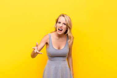 Genç sarışın kadın kızgın, sinirli ve hayal kırıklığına uğramış görünüyor. Turuncu duvara karşı senin neyin var? 