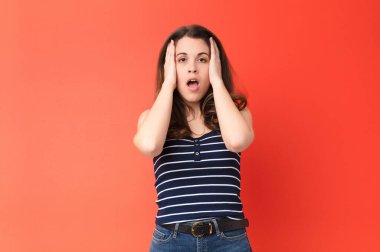 Genç ve güzel bir kadın hoş olmayan bir şekilde şok olmuş, korkmuş ya da endişeli görünüyor. Ağzı sonuna kadar açık ve iki kulağını da kırmızı duvara dayamış.
