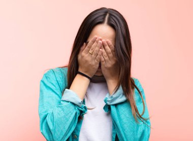 Genç, güzel bir kadın üzgün, hayal kırıklığına uğramış, gergin ve depresif, iki eliyle yüzünü kapatmış, pembe duvara karşı ağlıyor.