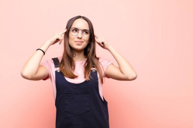 Genç ve güzel bir kadın konsantre olmuş ve bir fikir üzerinde kafa yoruyor. Pembe duvara karşı bir meydan okuma veya soruna bir çözüm hayal ediyor.