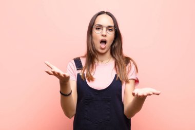 Genç ve güzel bir kadın son derece şaşkın, şaşırmış, endişeli ve paniklemiş hissediyor. Pembe duvara karşı stresli ve dehşetli bir bakışla bakıyor.