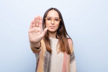 Genç ve güzel bir kadın ciddi, sert, hoşnutsuz ve kızgın görünüyor. Avuç içini açıp mavi duvara karşı durduğunu gösteriyor.