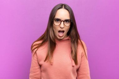 Genç ve güzel bir kadın çok şaşırmış ya da şaşkın görünüyor, ağzı açık bakıyor ve mor duvara karşı 