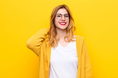 Genç, güzel sarışın kadın neşeli ve kendinden emin bir şekilde gülüyor sarı duvarın karşısında mutlu, samimi bir gülümseme ile.