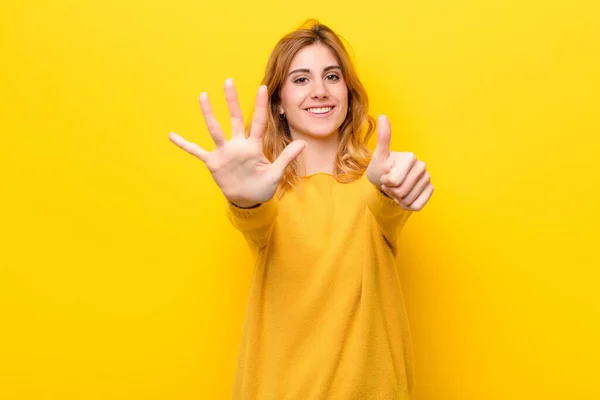 若いかなりブロンドの女性は笑顔で友好的に見える前方に手で6番目または6番目を示し黄色の壁に対してカウントダウン — ストック写真