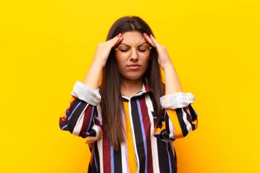 Genç ve güzel bir kadın stresli ve hayal kırıklığına uğramış görünüyor. Baskı altında çalışıyor ve sarı duvara karşı sorunlarla boğuşuyor.