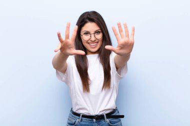 Genç, güzel bir kadın gülümsüyor ve dost canlısı görünüyor. 9 ya da 9 numarayı gösteriyor.