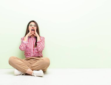 Genç, güzel bir kadın mutlu, heyecanlı ve pozitif hissediyor. Elleri ağızda bağırıyor, yerde otururken bağırıyor.