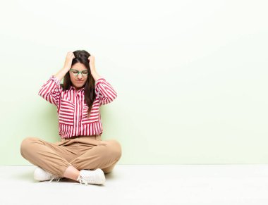 Genç, güzel bir kadın kendini stresli ve hayal kırıklığına uğramış hissediyor, elele tutuşuyor, yorgun, mutsuz ve migreniyle yerde oturuyor.