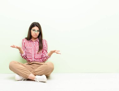 Genç ve güzel bir kadın şaşkın ve şaşkın hissediyor. Doğru cevap ya da karardan emin değil. Yerde oturarak bir seçim yapmaya çalışıyor.