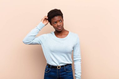 Genç, güzel, siyah kadın duyguları şaşkın ve kafası karışmış, başını kaşıyor ve yan tarafa bakıyor.