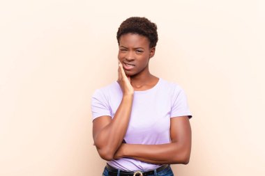 Genç, güzel, siyah bir kadın yanak tutuyor ve ağrılı diş ağrısı çekiyor, hasta, sefil ve mutsuz hissediyor, dişçi arıyor.