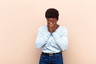 Genç, güzel siyah kadın üzgün, hayal kırıklığına uğramış, gergin ve depresif, iki eliyle yüzünü kaplayan, ağlayan