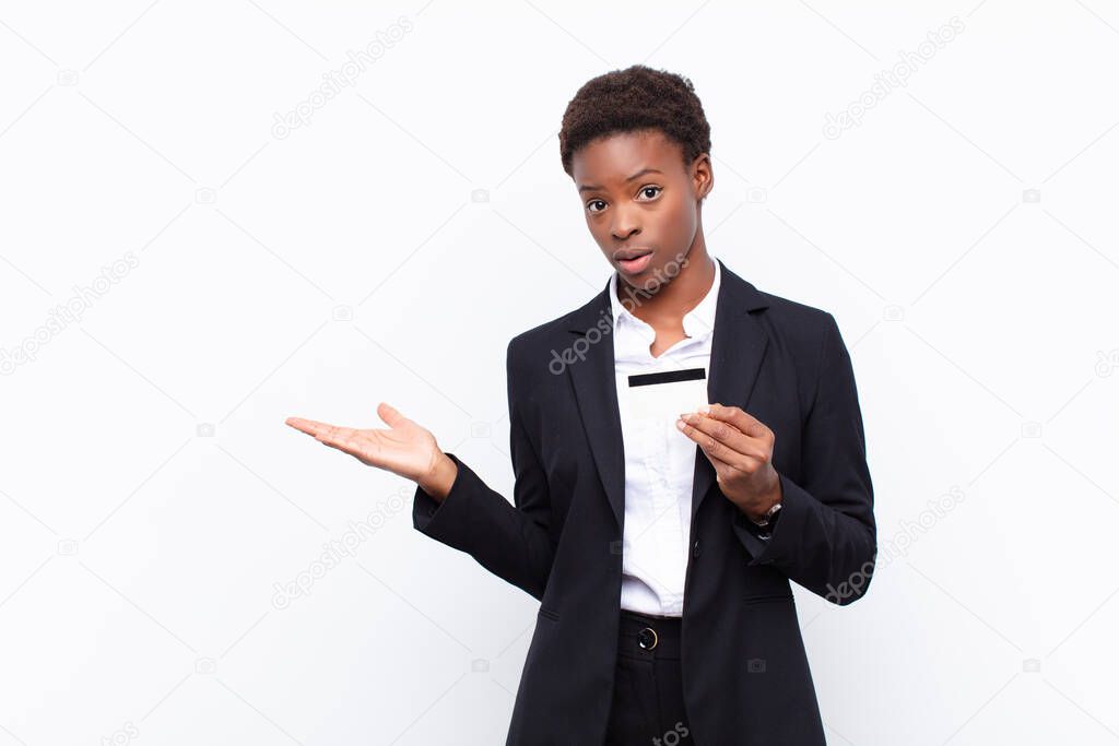 young pretty black womanlooking surprised and shocked, with jaw dropped holding an object with an open hand on the side holding a credit card