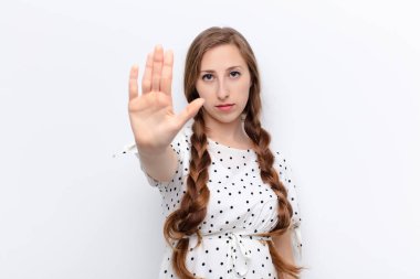 Genç sarışın kadın ciddi, sert, hoşnutsuz ve kızgın görünüyor. Avuç içini açıp beyaz duvara karşı jest yapıyor.