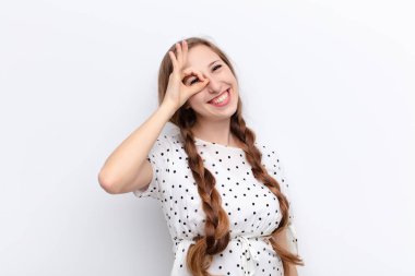 Genç sarışın kadın mutlu bir şekilde gülümsüyor, şaka yapıyor ve gözetleme deliğinden bakıyor, beyaz duvara karşı sırları gözetliyor.