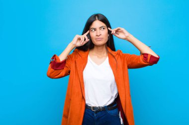 Genç, güzel, Latin bir kadın, kafası karışmış ya da şüpheye düşmüş, bir fikre odaklanmış, çok düşünüyor, düz duvara karşı uzayı kopyalamak istiyor.