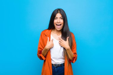 Genç, güzel, Latin bir kadın mutlu, şaşırmış ve gururlu hissediyor. Heyecanlı ve şaşırmış bir şekilde duvara bakıyor.