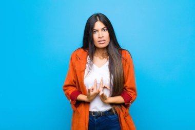 Genç, güzel, Latin bir kadın, kafası karışık ve tuhaf bir bakışla kendini işaret ediyor. Düz duvara karşı seçildiği için şaşırmış ve şaşırmış görünüyor.