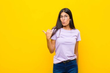 Genç ve güzel Latin kadın inançsızlıktan şaşkın şaşkın bakıyor, yan taraftaki objeyi işaret ediyor ve 