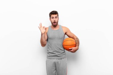 Genç yakışıklı adam şok olmuş, şaşırmış ve şaşırmış hissediyor. Onaylıyor. İki eliyle basketbol topu tutuyor..