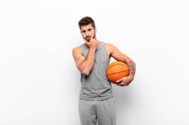 Genç yakışıklı adam ciddi, düşünceli ve güvensiz görünüyor, bir kolu çapraz ve çene üzerinde, basketbol topu tutan seçenekleri tartıyor..