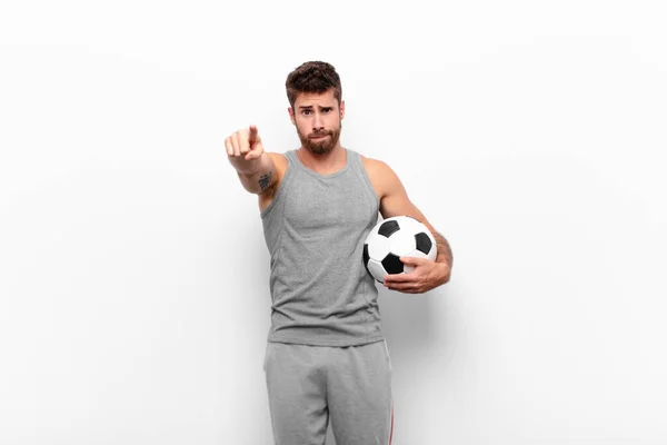 若いハンサムな男は指と怒りの表情でカメラを前に向けサッカーボールを保持するあなたの義務を行うように指示します — ストック写真