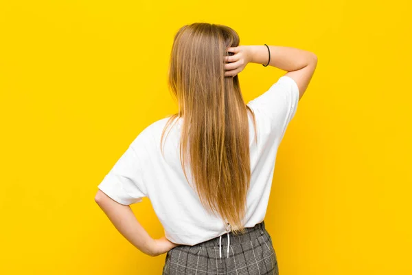 年轻的金发女人思考或怀疑 感到困惑和困惑 背对着橙色的墙看或后视镜 — 图库照片