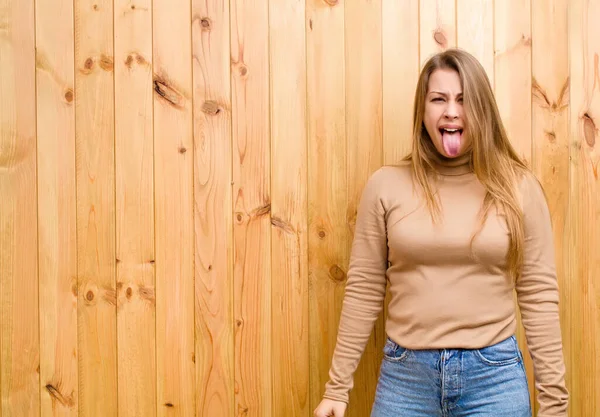 陽気で屈託のない反抗心を持ち冗談を言いながら舌を出す若いブロンド女性 — ストック写真
