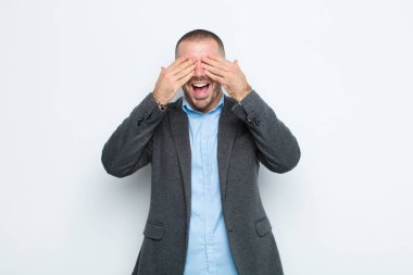 Genç işadamı gülümsüyor ve mutlu hissediyor, iki eliyle gözlerini kapatıyor ve düz duvara karşı inanılmaz bir sürpriz bekliyor.