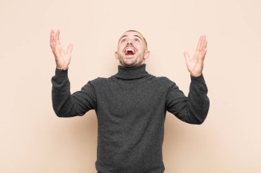 Genç yakışıklı adam kendini mutlu, şaşkın, şanslı ve şaşırmış hissediyor, zaferi kutlarken iki elini de havaya kaldırıp düz duvara yaslanıyor.