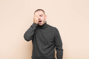 Genç ve yakışıklı bir adam uykulu, sıkılmış ve esniyor, baş ağrısı ve bir eli düz duvara karşı yüzünün yarısını kaplıyor.