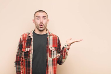 Genç yakışıklı adam şaşırmış ve şoka uğramış görünüyor, çenesi düşmüş ve düz duvara karşı eli açık bir nesne tutuyor.