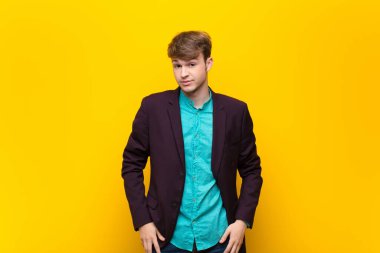 Genç sarışın adam gururlu, kendine güvenen, havalı, küstah, küstah, gülümseyen, başarılı, yassı duvara karşı izole edilmiş hissediyor.