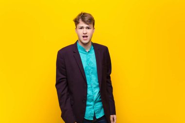 Genç sarışın adam korkmuş ve şok olmuş hissediyor, ağzı ardına kadar açık, şaşırmış bir şekilde duvara yaslanmış.