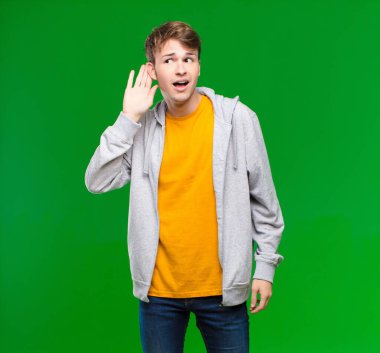 Genç sarışın adam gülümsüyor, tuhaf bir şekilde yan tarafa bakıyor, dedikoduları dinlemeye çalışıyor ya da kroma anahtar duvarına karşı bir sırrı duymaya çalışıyor.