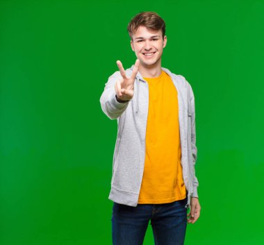 Genç sarışın adam gülümsüyor ve arkadaş canlısı görünüyor, iki numarayı gösteriyor, elini ileri uzatıyor, kroma anahtarına karşı geri sayıyor.