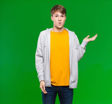 Genç sarışın adam şaşırmış ve şoka uğramış görünüyor, çenesi düşmüş, kolları açık bir objeyi kroma tuşuna karşı tutuyor.