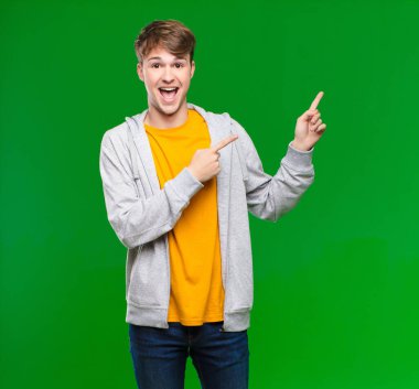 Genç sarışın adam şaşkın ve şaşırmış hissediyor, şok olmuş bir ifadeyle gülümsüyor ve kroma anahtarına karşı kenarı işaret ediyor.