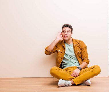 Genç Arap adam ciddi ve meraklı görünüyor, dinliyor, gizli bir konuşma ya da dedikodu duymaya çalışıyor, yerde oturup gizlice dinliyor.