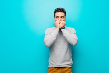 Genç Arap adam endişeli, gergin, stresli ve korkmuş görünüyor, tırnaklarını yiyor ve düz duvara karşı yanal kopyalama alanı arıyor.