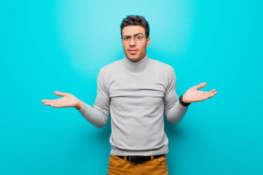 Şaşkın, kafası karışmış ve stresli görünen genç bir Arap, farklı seçenekler arasında merak içinde, düz duvara karşı kararsız hissediyor.