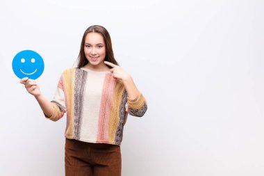 Beyaz duvarda gülümseyen yüz ikonu olan genç sarışın güzel kız.